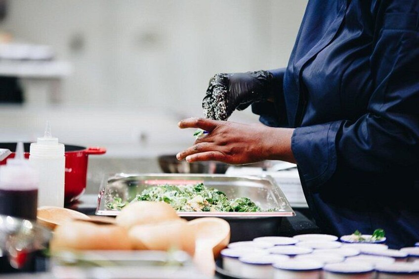 A person in a blue uniform preparing food, with a red pot and a container of green vegetables on the counter. 4
