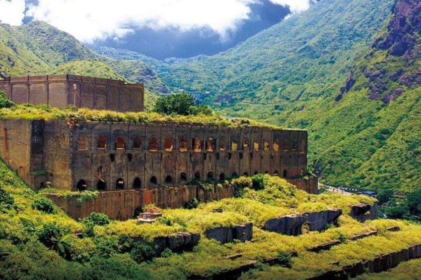 Un bâtiment abandonné, doté de fenêtres en arc, entouré d’une végétation luxuriante et bordé de montagnes. 4