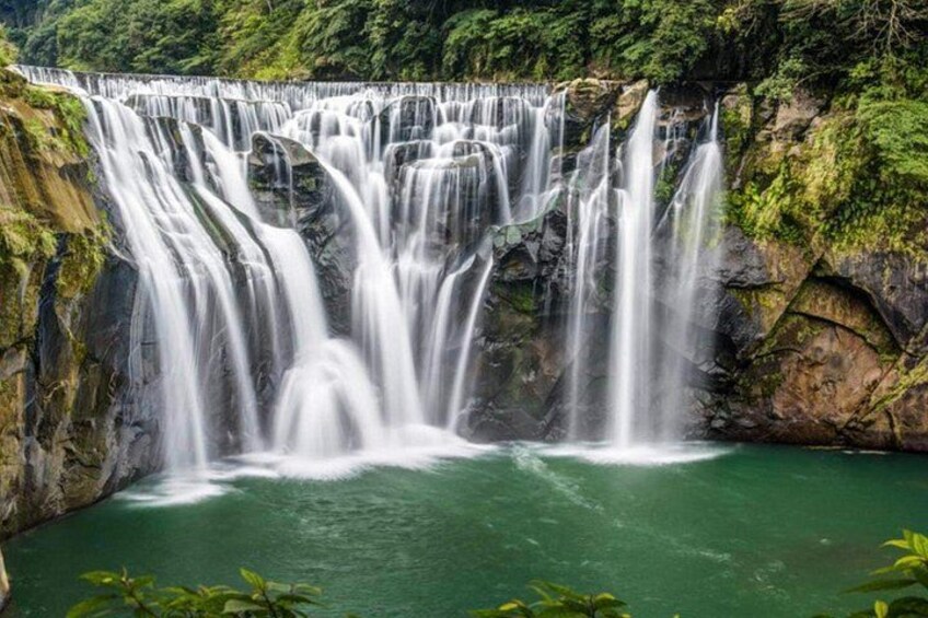 Une cascade à plusieurs niveaux dévalant les rochers et se jetant dans une étendue d’eau verdoyante, le tout entouré d’une végétation luxuriante. 2