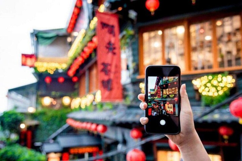 Une main tenant un téléphone intelligent sur lequel est affichée une photo d’un bâtiment traditionnel orné de lanternes rouges et d’une banderole rouge. 5