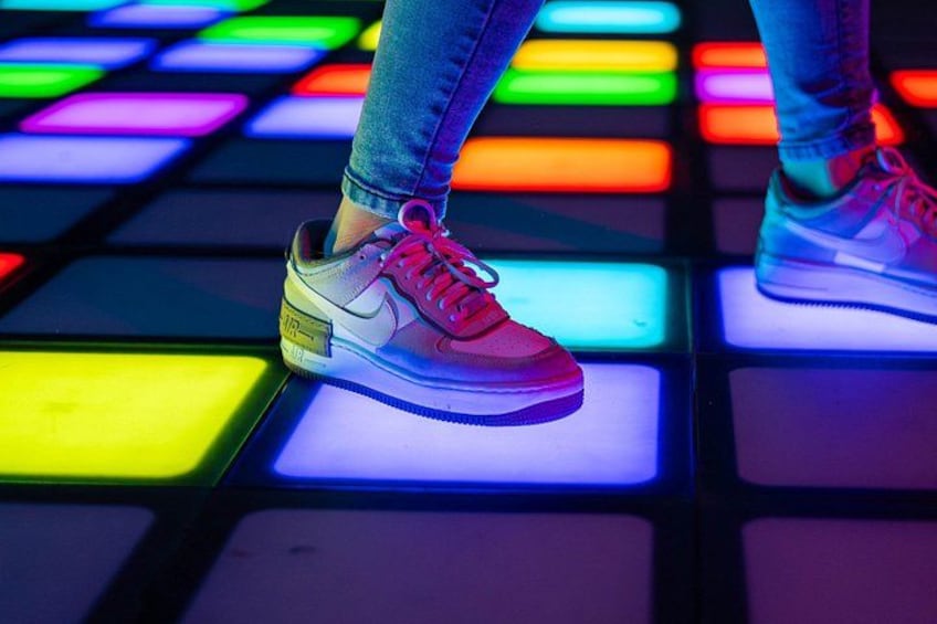 A person standing on a floor with illuminated tiles in various colors. 3