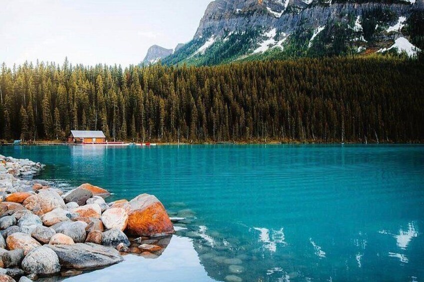 A turquoise lake with a wooden cabin and a dense forest of coniferous trees. 4