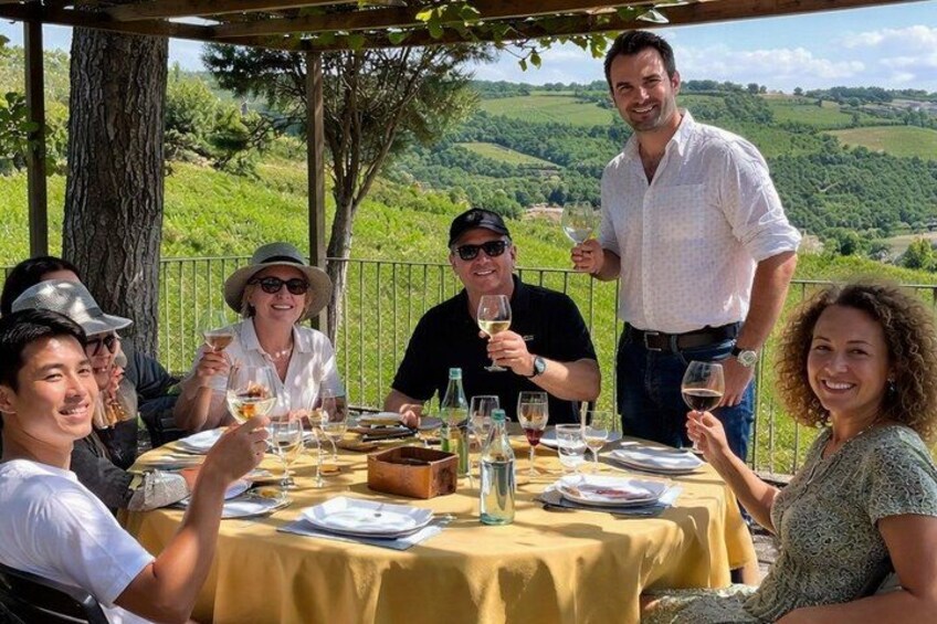 A group of people dining outdoors with a table set for a meal, surrounded by a lush landscape. 1