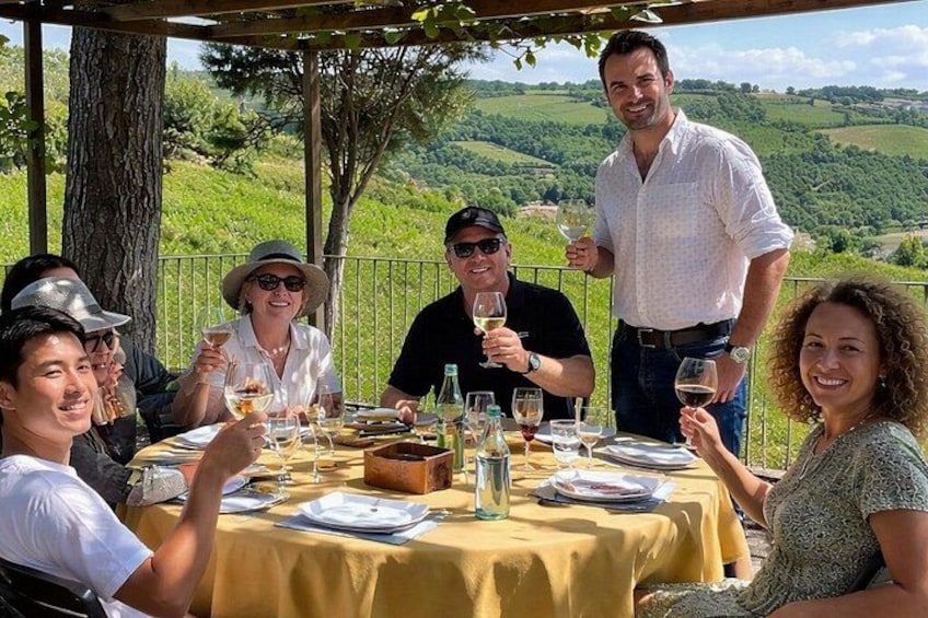 Un grupo de personas cenando al aire libre, con un viñedo de fondo. 1