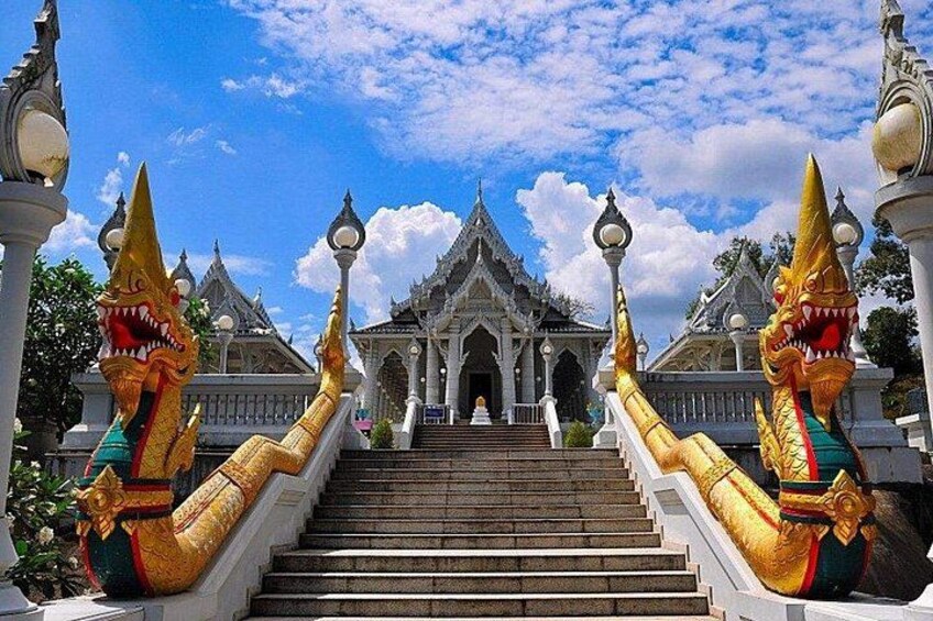 Een tempel met versierde gouden naga-beelden bij de ingang, een trap die naar de tempel leidt en traditionele Thaise architectuur op de achtergrond. 1