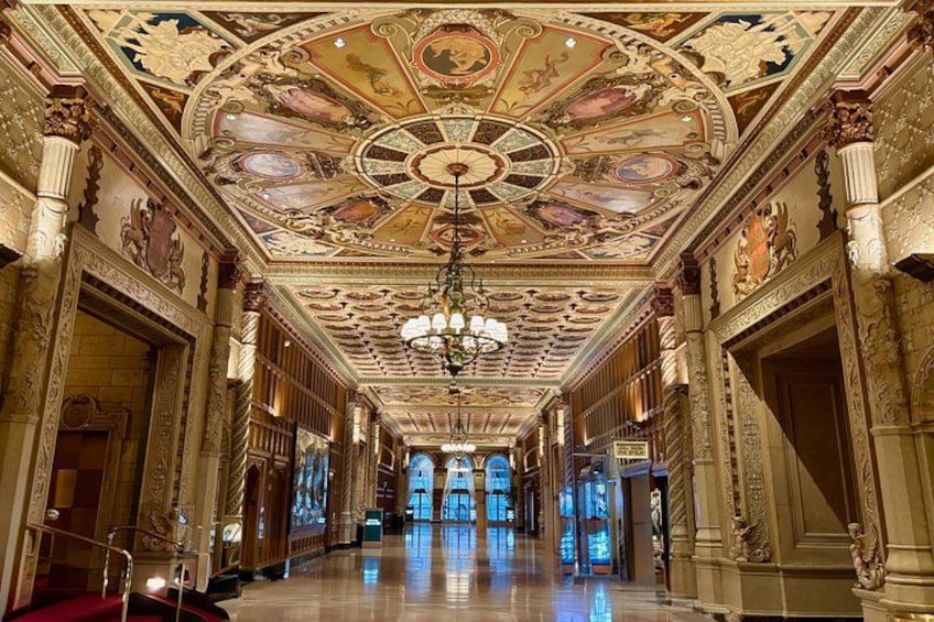 An ornate hallway with a detailed ceiling, columns, and a chandelier. 2