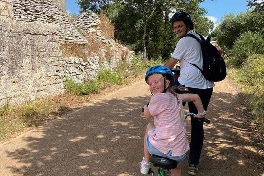 Une personne à vélo circule sur un chemin de terre, avec un mur de pierres d’un côté. 4