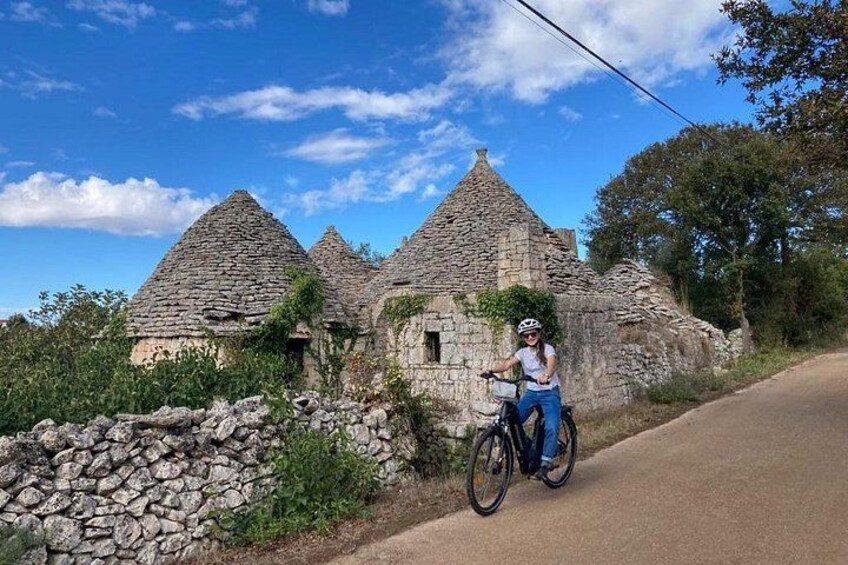 Un bâtiment en pierre surmonté d’un toit conique, un cycliste sur une piste pavée et un mur de pierre. 2