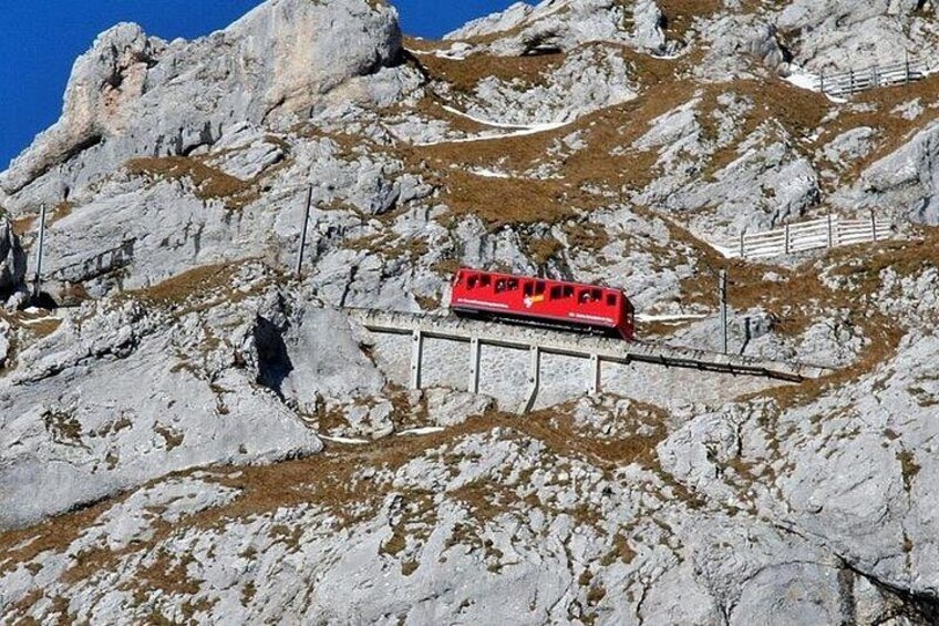 Un treno rosso su un binario montano, con terreno roccioso e chiazze di neve. 4