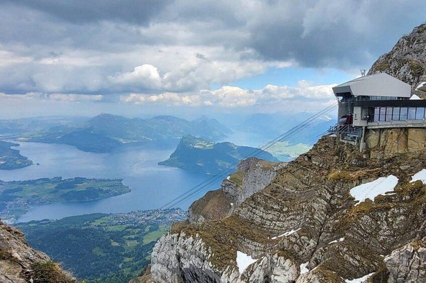 Una vista panoramica su una montagna, con una baita, un lago e montagne sullo sfondo. 1