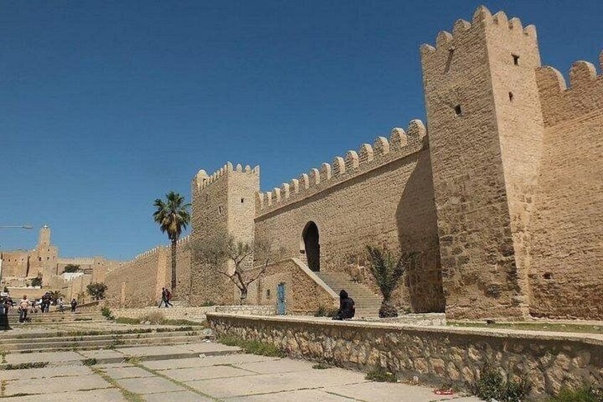 Muralla de piedra histórica con almenas, palmeras y un cielo azul despejado. 2