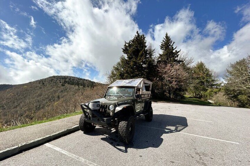 A 4x4 vehicle parked in a parking lot with a mountainous landscape in the background. 2