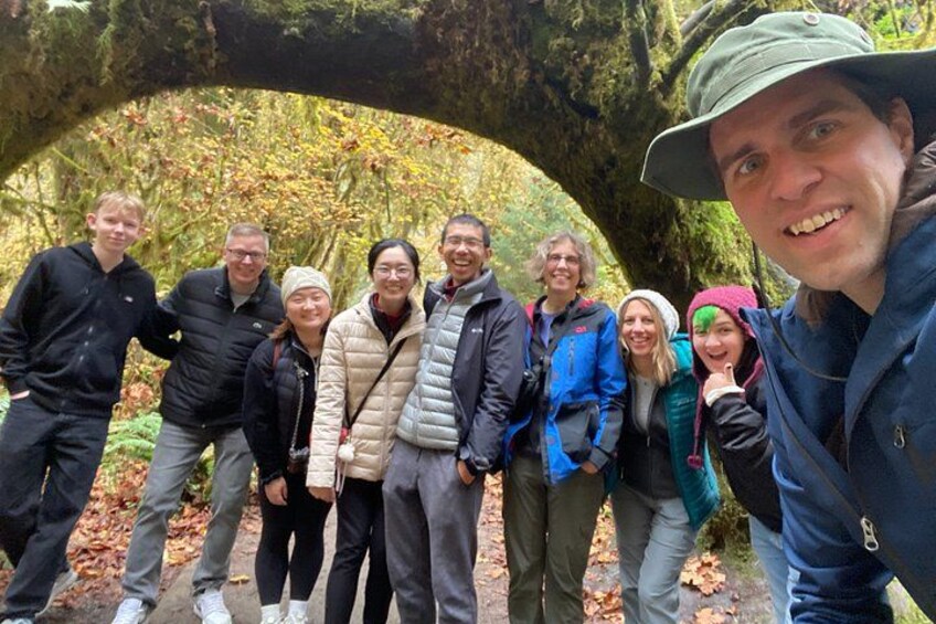 A group of people standing under a large tree with a natural arch formation. 3