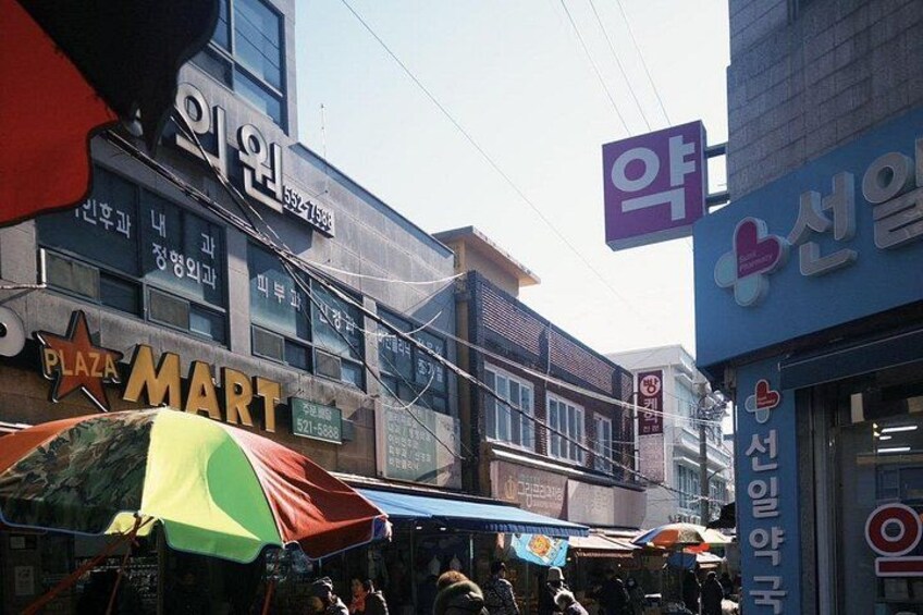 A busy street with various shops and signs, including a pharmacy and a supermarket. 1