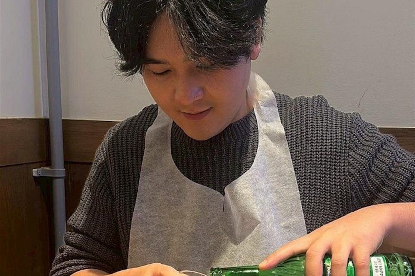 A person wearing a bib, seated at a table with a bottle of green liquid. 3