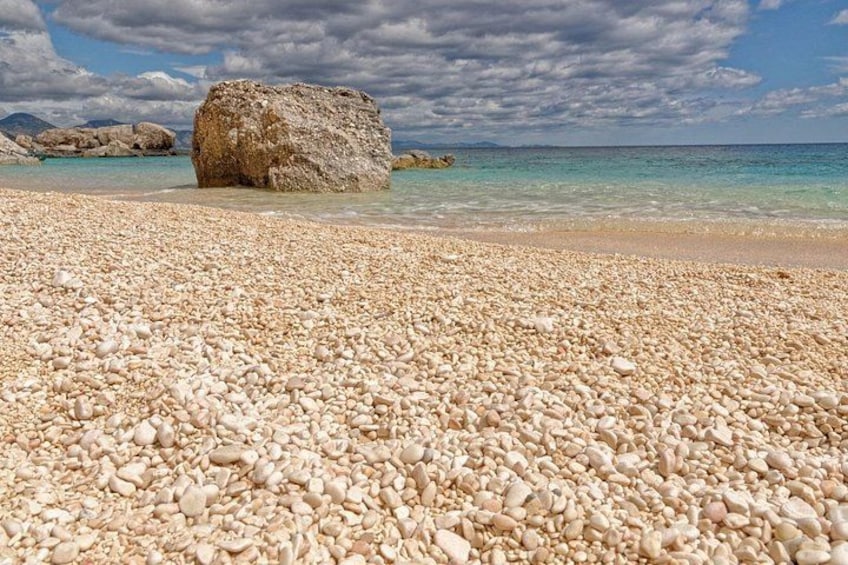 A pebble beach with clear turquoise water and a large rock in the distance. 2