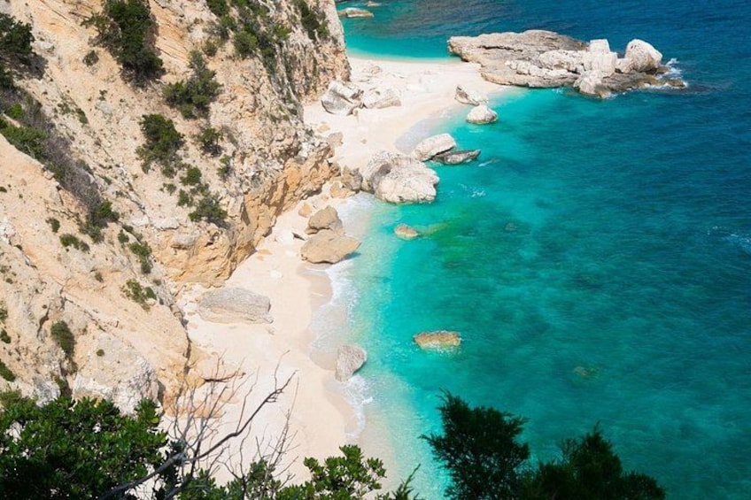 A coastal landscape with a sandy beach, clear turquoise waters, and rocky outcrops. 4