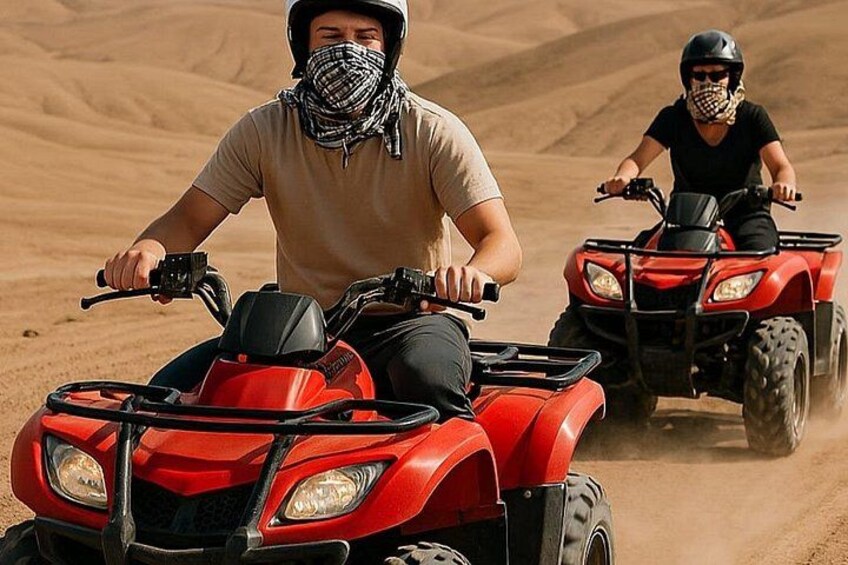 Two people riding red quad bikes on a sandy terrain. 5