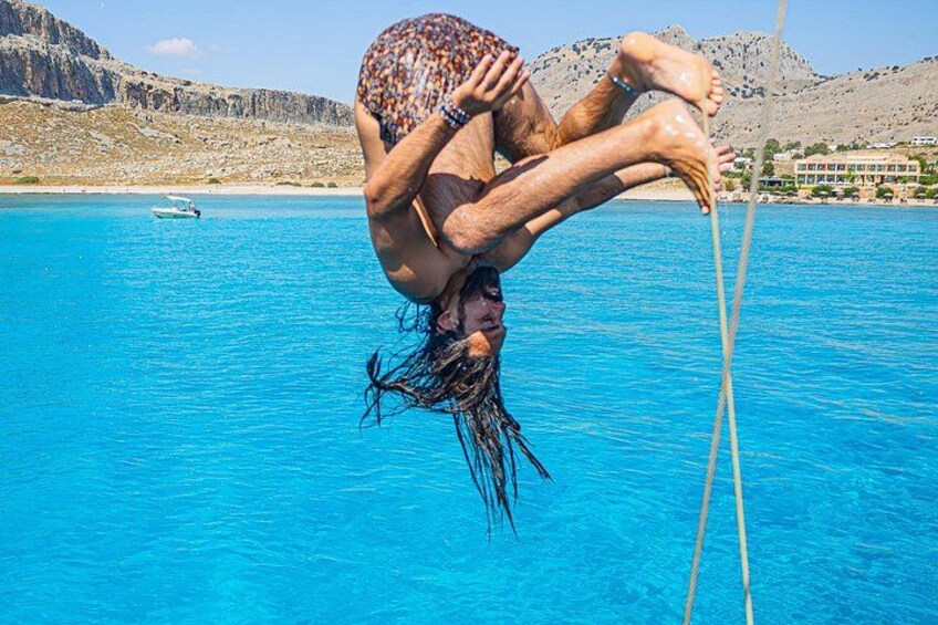 Eine Person macht eine Handstand in einem klaren, blauen Pool. Im Hintergrund sind ein Boot und eine felsige Landschaft zu sehen. 5