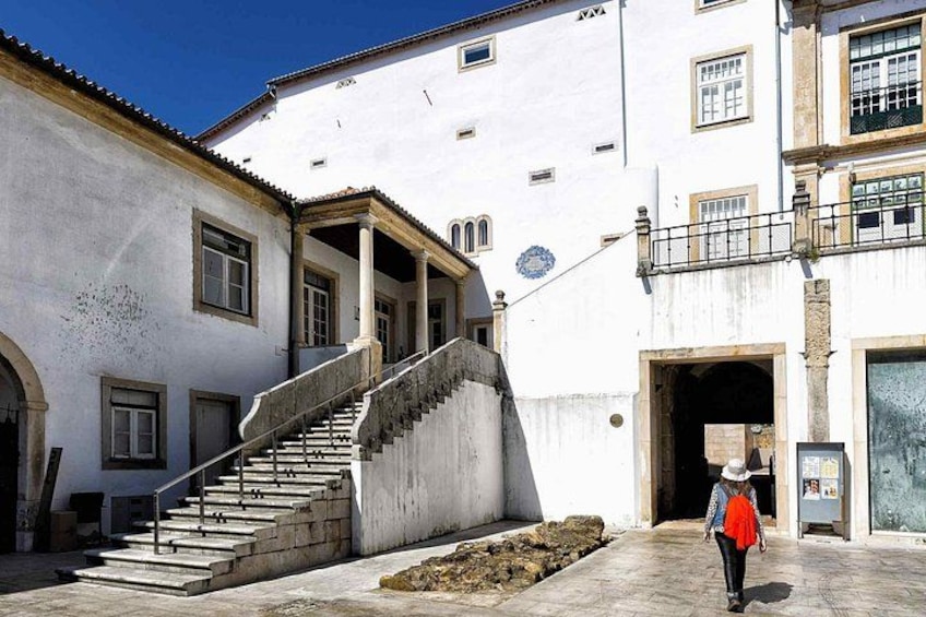 Un edificio bianco con una scala che conduce a un'area coperta, una persona che cammina, e un cielo azzurro intenso. 4