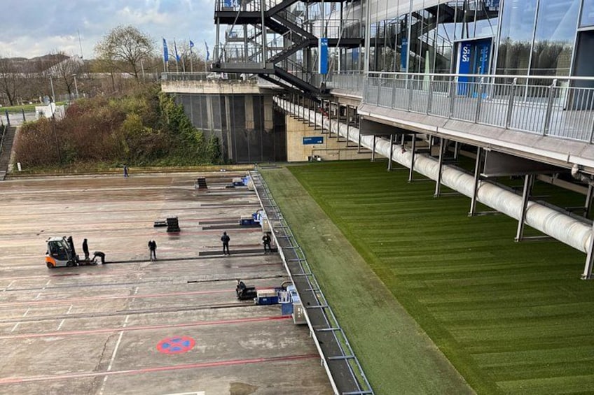 A parking lot with a green field, a building with a glass facade, and a pedestrian bridge. 4