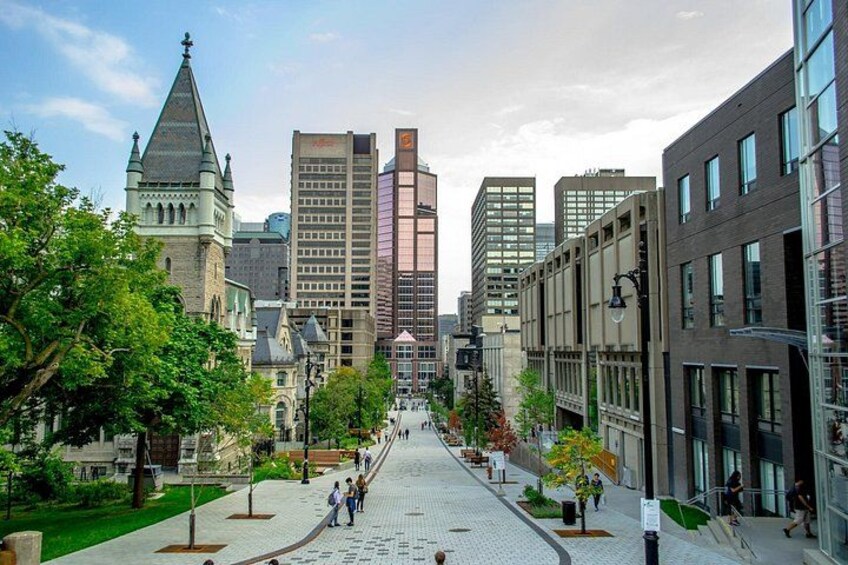 A city street lined with modern and historic buildings, a prominent tower, and a tree-lined sidewalk. 3