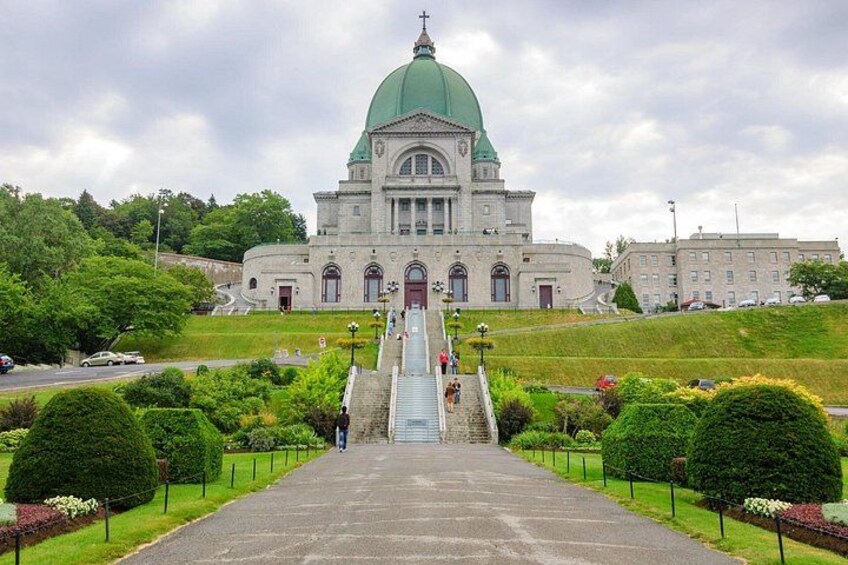 A large building with a green dome, a staircase leading to the entrance, and a well-maintained garden with trimmed bushes. 5
