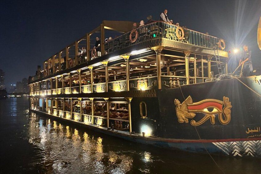 Een grote, verlichte rivierboot met meerdere dekken en passagiers. 2