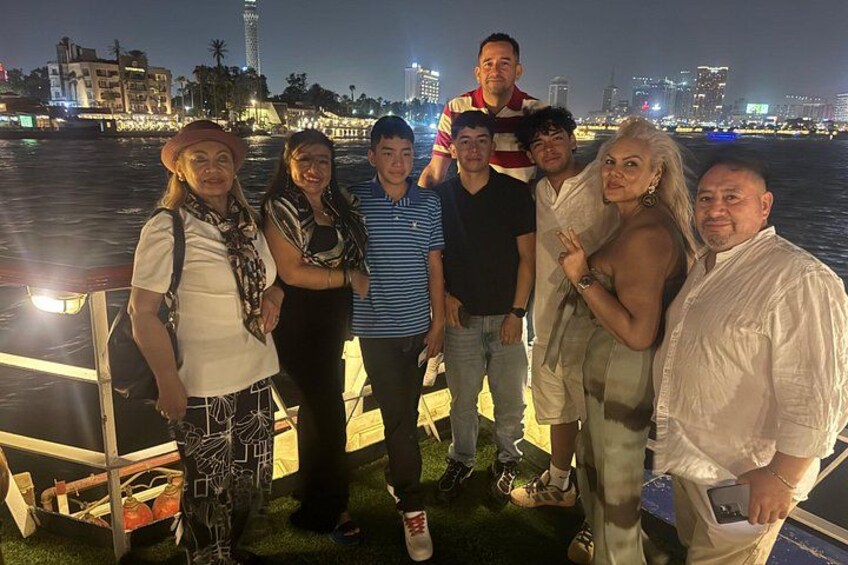 Een groep mensen staat op een steiger in de nacht, met een stadsachtergrond op de achtergrond. 3