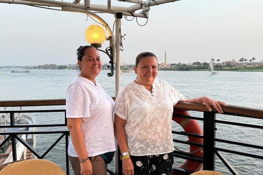Twee mensen in een boot, met een stadsgezicht en een zeilboot op de achtergrond. 3
