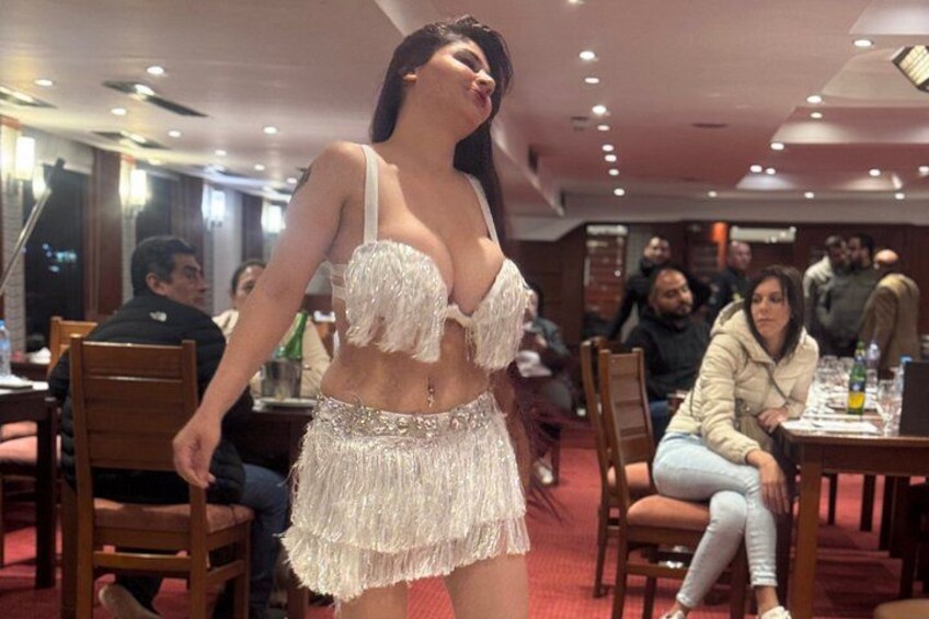 Een persoon in een witte outfit met franjes in een restaurant met houten stoelen en tafels. 2