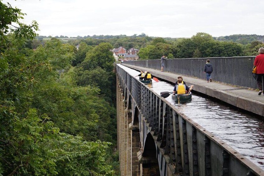 A bridge with people riding in boats, surrounded by greenery. 4