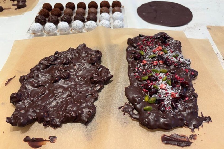 Two chocolate-covered desserts on parchment paper, one with nuts and dried fruits, and another with a rough texture. 3