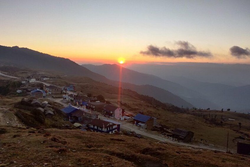 A village at sunset with a clear sky, a prominent sun, and distant mountains. 5