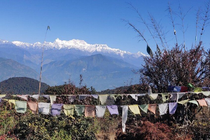 A mountainous landscape with snow-capped peaks in the background, a string of colorful prayer flags in the foreground, and a clear blue sky. 4
