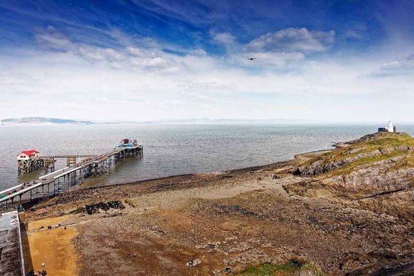 A coastal landscape with a pier extending into the water, rocky shore, and a lighthouse in the distance. 2