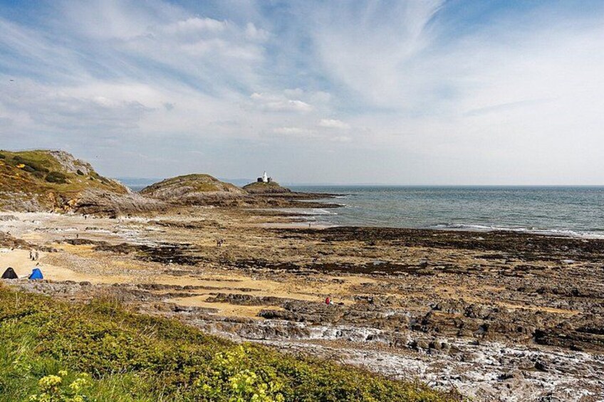 A rocky beach with a lighthouse, tents, and a grassy foreground. 4