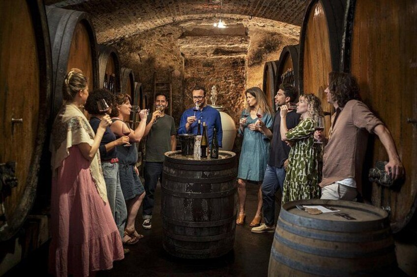 A group of people in a dimly lit cellar with wooden barrels and stone walls. 3