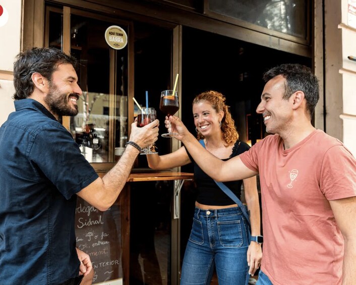Three people toasting with drinks outside a bar. 1
