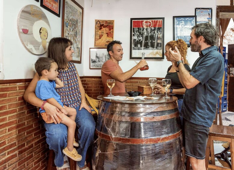 A group of people sitting around a wooden barrel table in a restaurant with vintage posters on the wall. 5
