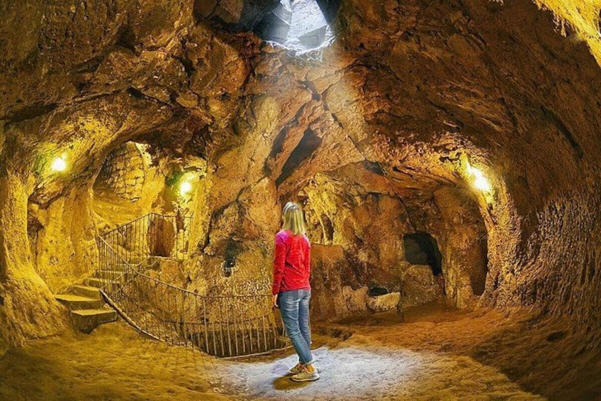 A person standing in a cave with a spiral staircase and a skylight. 3