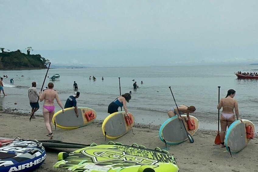 People on a beach with surfboards and paddleboards, some in the water and others on the shore. 4
