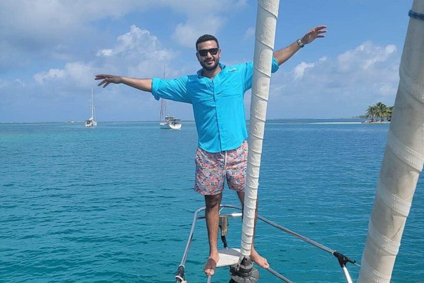 A person standing on a boat with a clear blue sea and distant islands in the background. 1