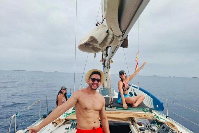 A sailboat with a person standing at the bow, another person sitting at the stern, and a third person in the background. 2