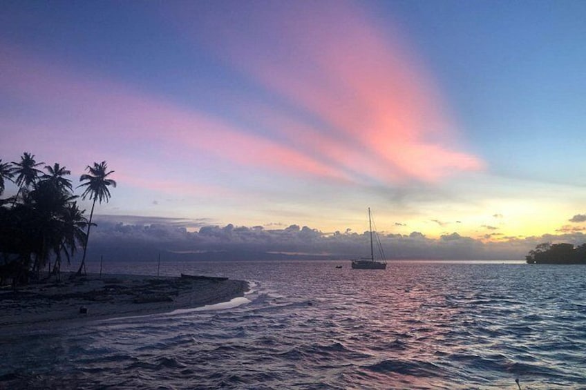 A beach with palm trees, a sailboat, and a sunset. 3