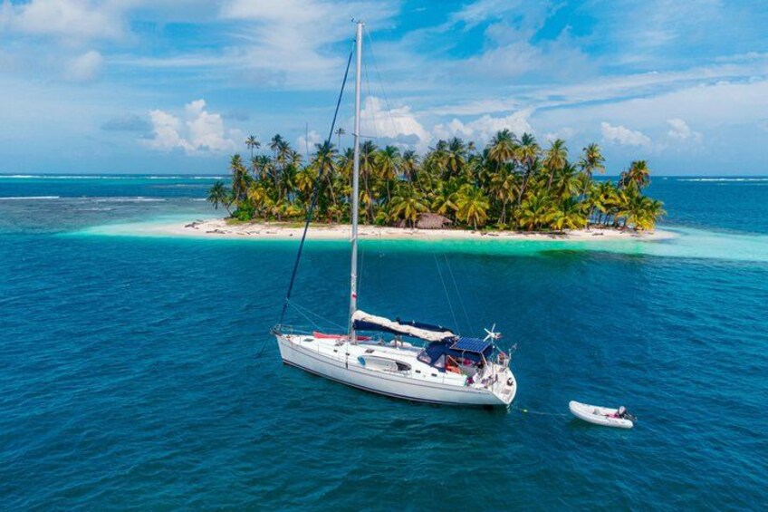 A sailboat anchored near a tropical island with palm trees. 1