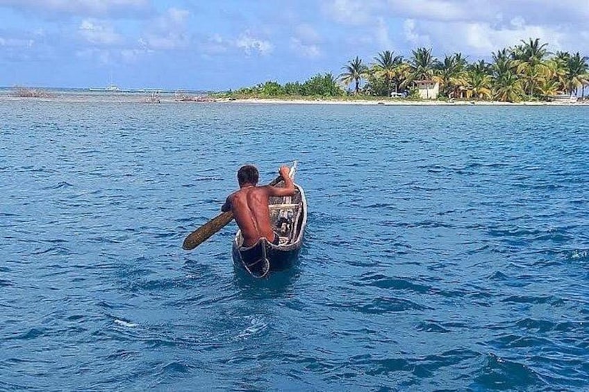 A man paddling a canoe on a calm sea with a tropical island in the background. 5