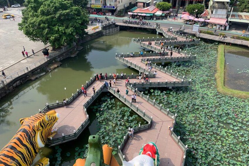 A riverside walkway with lily pads, a bridge, and a large tiger statue. 5