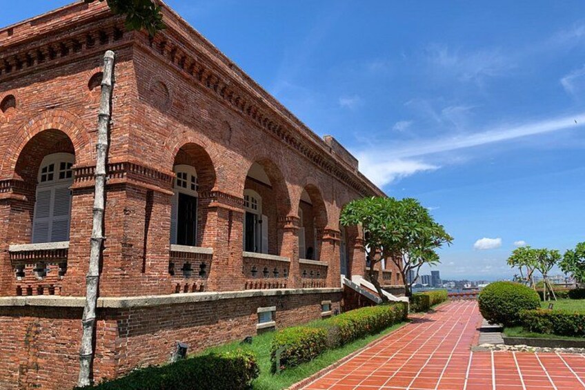 A brick building with arched windows and a red-tiled pathway. 3