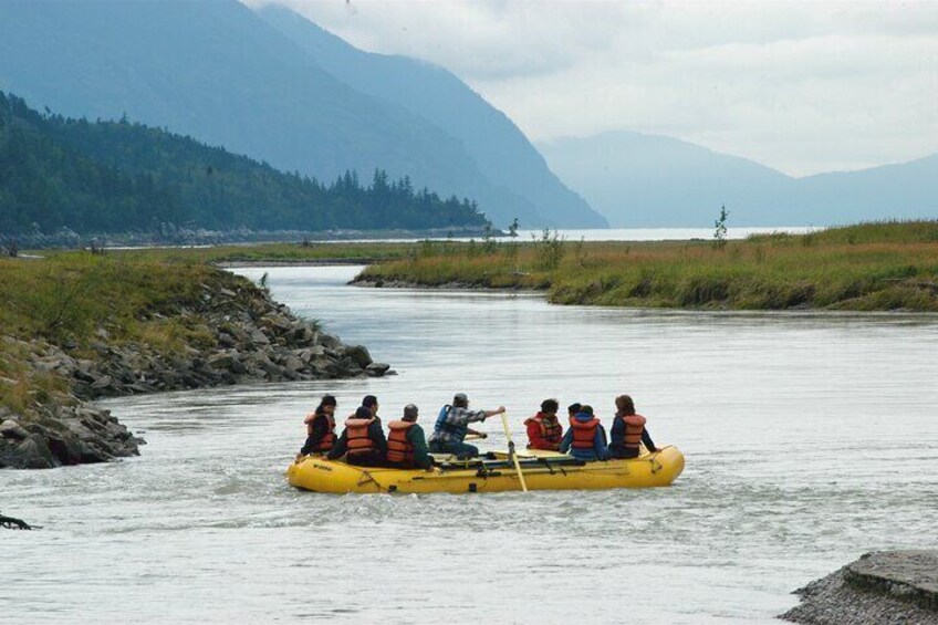 A group of people in a yellow raft on a river with mountains in the background. 5